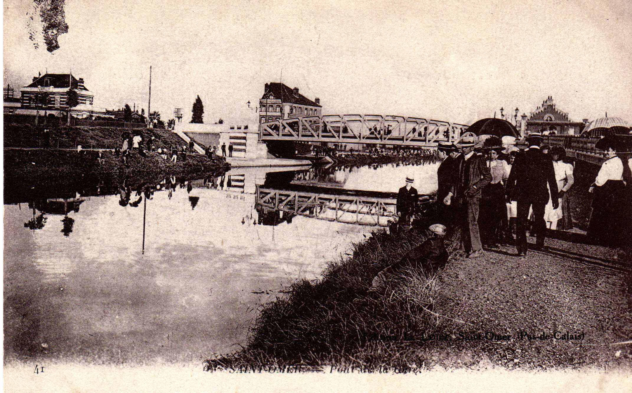 Au bord du canal, les danes avec leurs ombrelles et les messieurs en canotier. Au fond on aperçoit la passerelle qui enjambe le canal pour aller vers la gare.